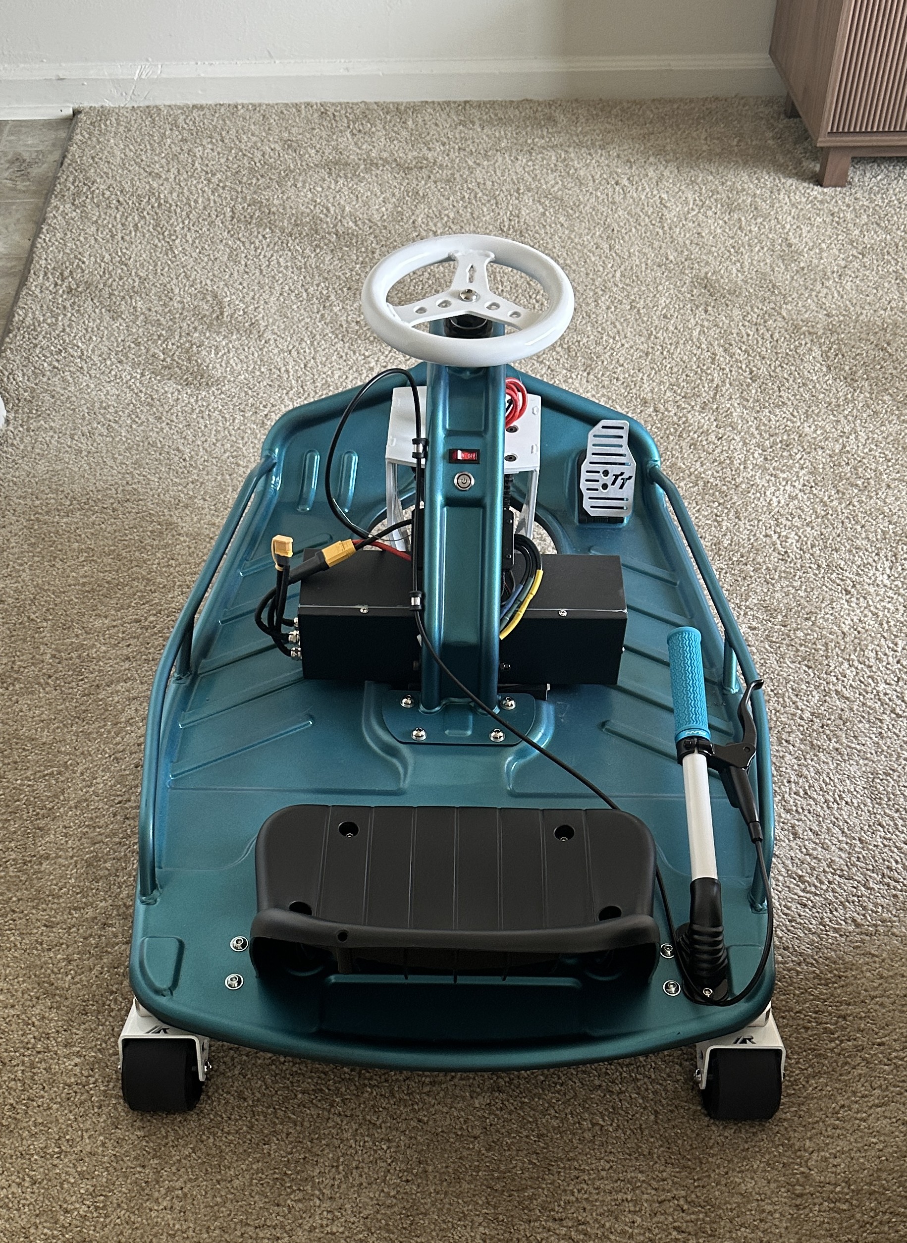 Electric drift kart with the motor controller and battery enclosures mounted to the deck, steering column, throttle pedal, and hand brake lever